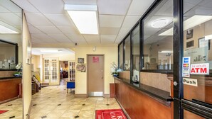 A hotel reception area with a reception desk, a 24-hour ATM, and a push button for the ATM. - Red Carpet Inn (Stamford)