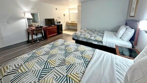 A hotel room with two beds, a desk with a computer, a TV, a dresser, and a bathroom visible through an open door. - Red Carpet Inn (Stamford)