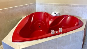 A red jacuzzi tub with a white towel and two bottles of shampoo. - Red Carpet Inn (Stamford)
