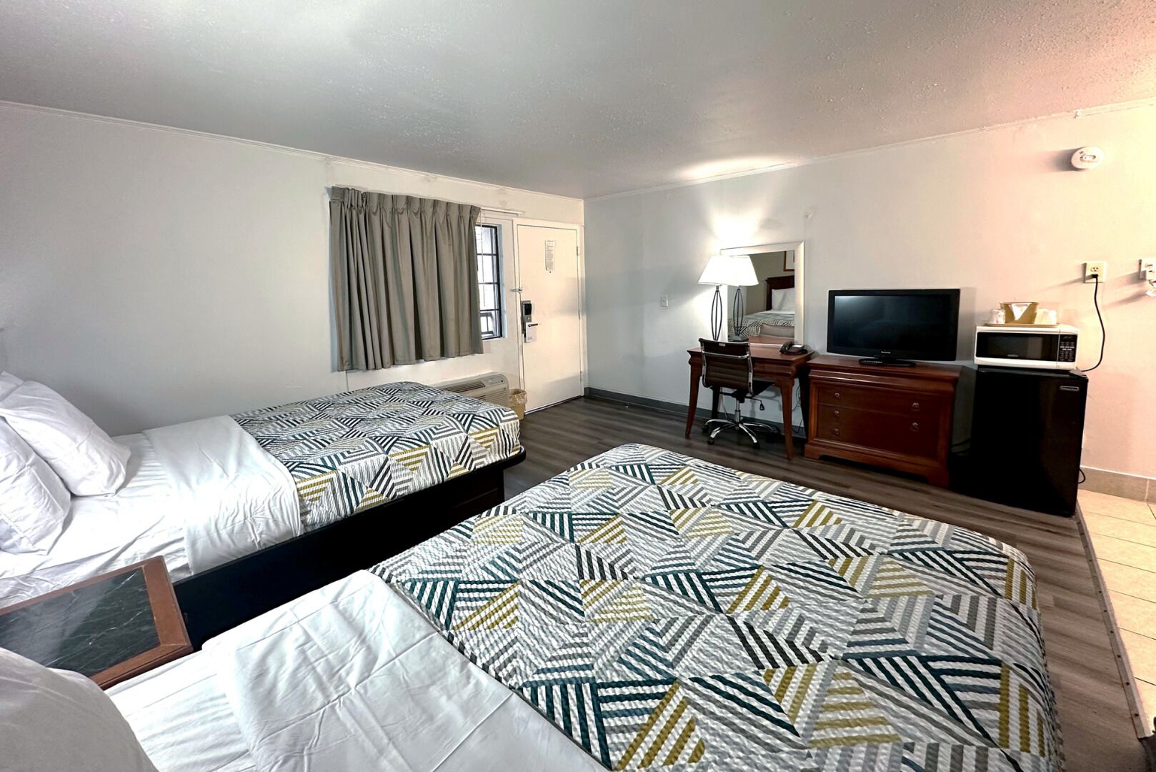 Habitación de hotel con dos camas, un escritorio con silla, televisor, microondas y un mueble pequeño.