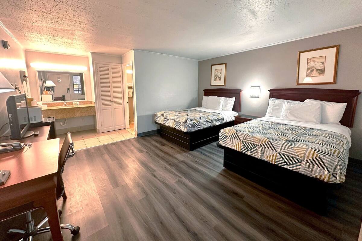 A hotel room with two beds, a desk with a computer, and a bathroom visible through an open door.