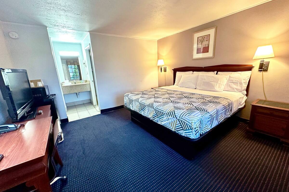 A hotel room with a bed, a desk, a television, and a bathroom visible through an open door.
