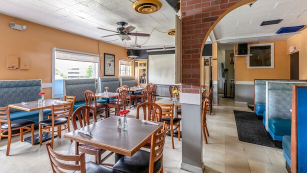 A restaurant with booths and tables, a ceiling fan, and a brick archway. - Red Carpet Inn (Stamford)