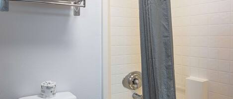 A bathroom with a toilet, a towel rack with towels, a shower curtain, and a bathtub.