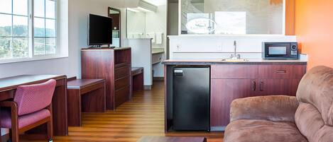 Un espacio habitable compacto con kitchenette, un sofá, un escritorio y una televisión.