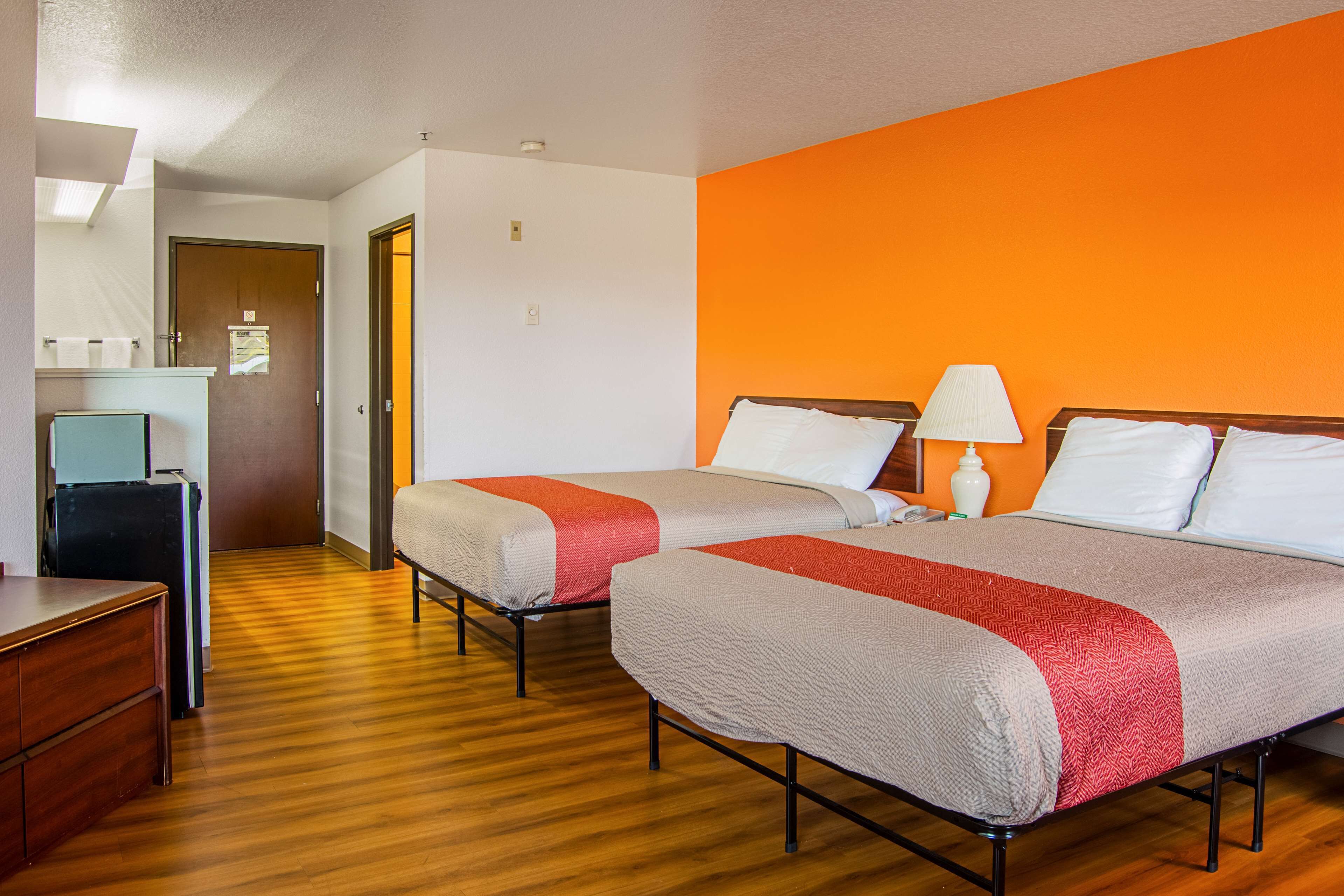 Une chambre d’hôtel avec deux lits, un plancher en bois, un bureau et une salle de bain visible au fond.