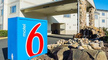 Une enseigne de motel avec le chiffre 6, un pilier en pierre et l’entrée d’un bâtiment.