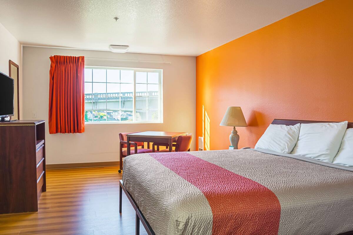 Ein Hotelzimmer mit Bett, Schreibtisch, Stuhl, Fernseher und einem Fenster mit Vorhängen.