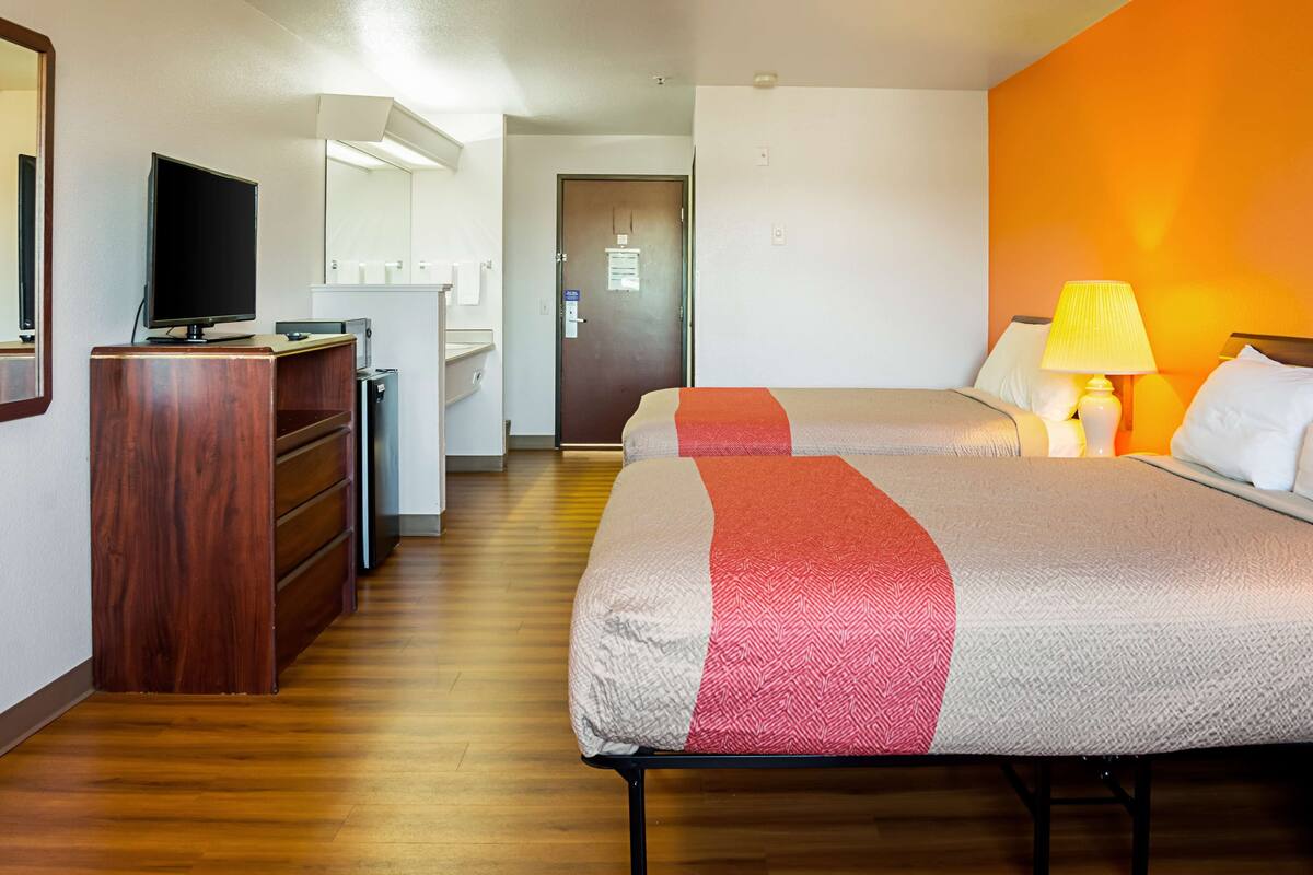 Ein Hotelzimmer mit zwei Betten, einem Schreibtisch mit Fernseher und einem durchgegangenen Tür sichtbaren Badezimmer.