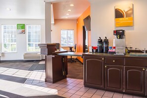 A modern hotel lobby with a reception desk, seating area, and a coffee machine.
