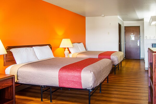 A hotel room with two beds, wooden flooring, and a bright orange wall.
