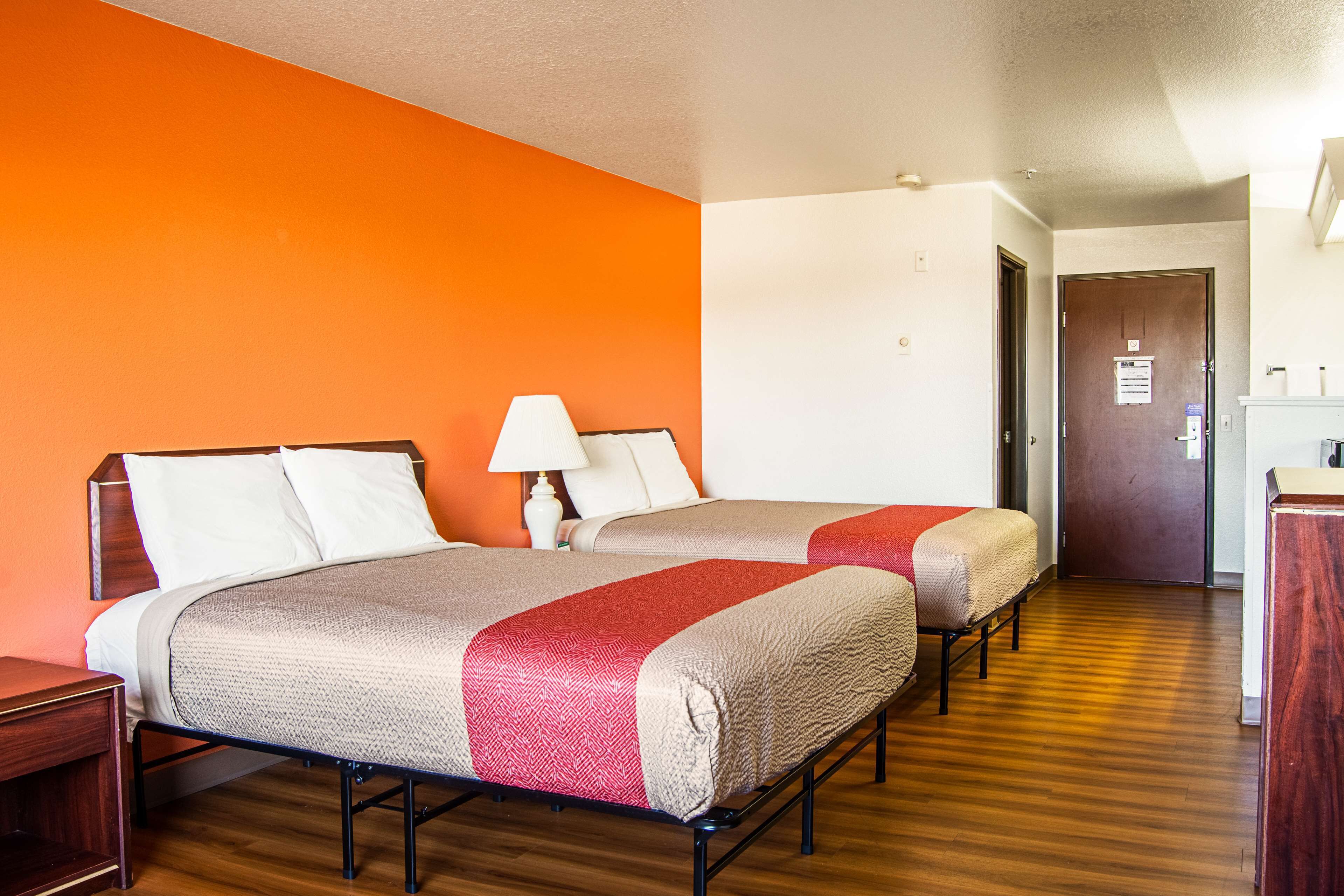 A hotel room with two beds, a wooden floor, and an orange accent wall.