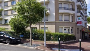 Un edificio residencial de varios pisos con balcones, un paso de peatones y un árbol en la parte delantera.