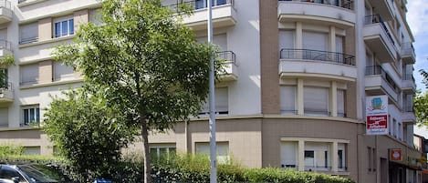 A multi-story residential building with balconies, a crosswalk, and a tree in front.