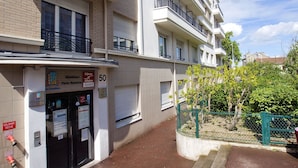 Un edificio residencial de varios pisos, con balcones, entrada a nivel de calle y un pequeño jardín.