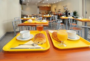 A breakfast setting with trays containing croissants, juice, and coffee cups. - Séjours & Affaires Paris Nanterre (Nanterre)