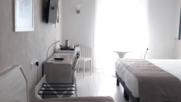 A hotel room with a bed, a desk with a chair, a television, and a window with curtains.