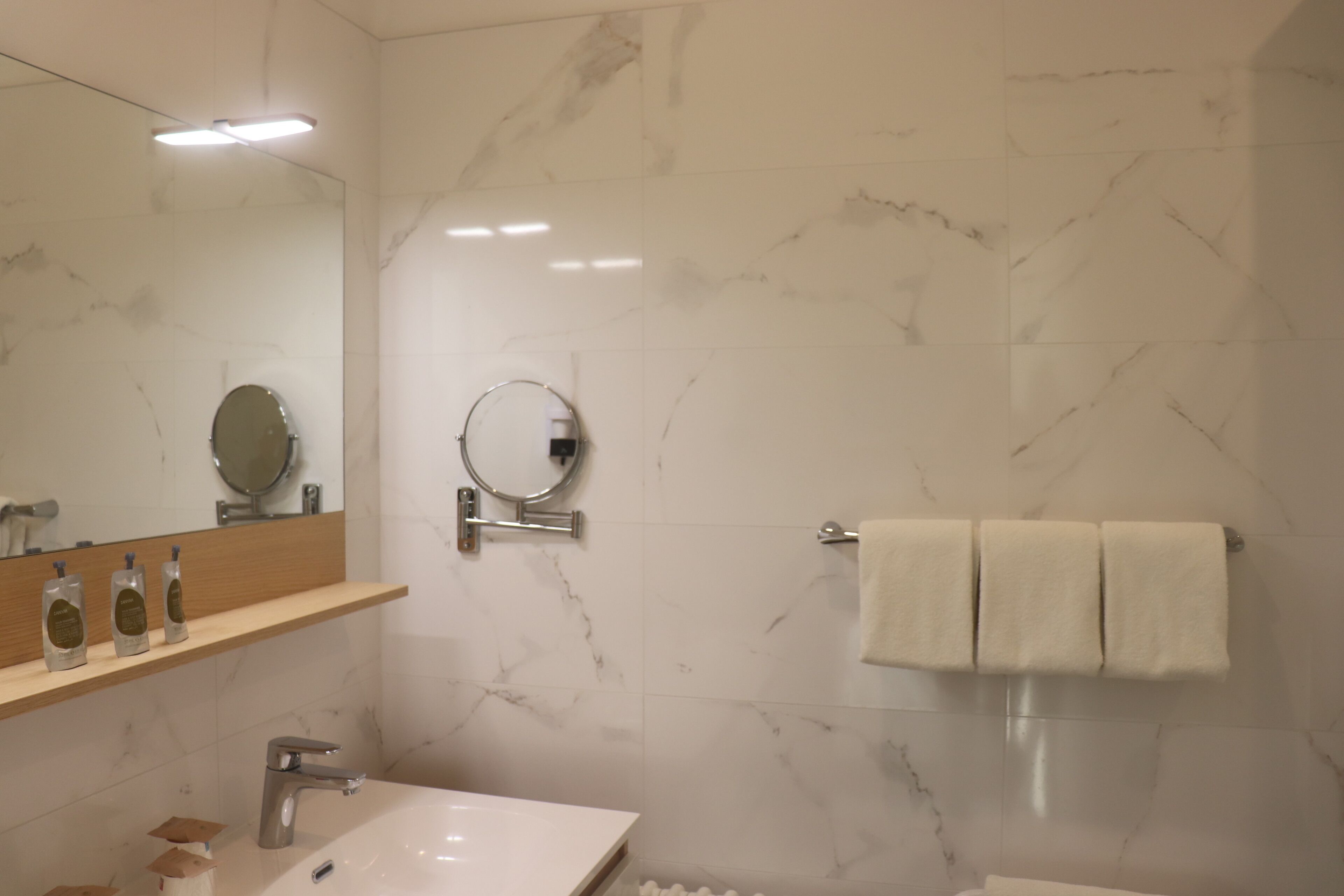 A modern bathroom with a marble wall, a sink with a mirror, and a towel rack.