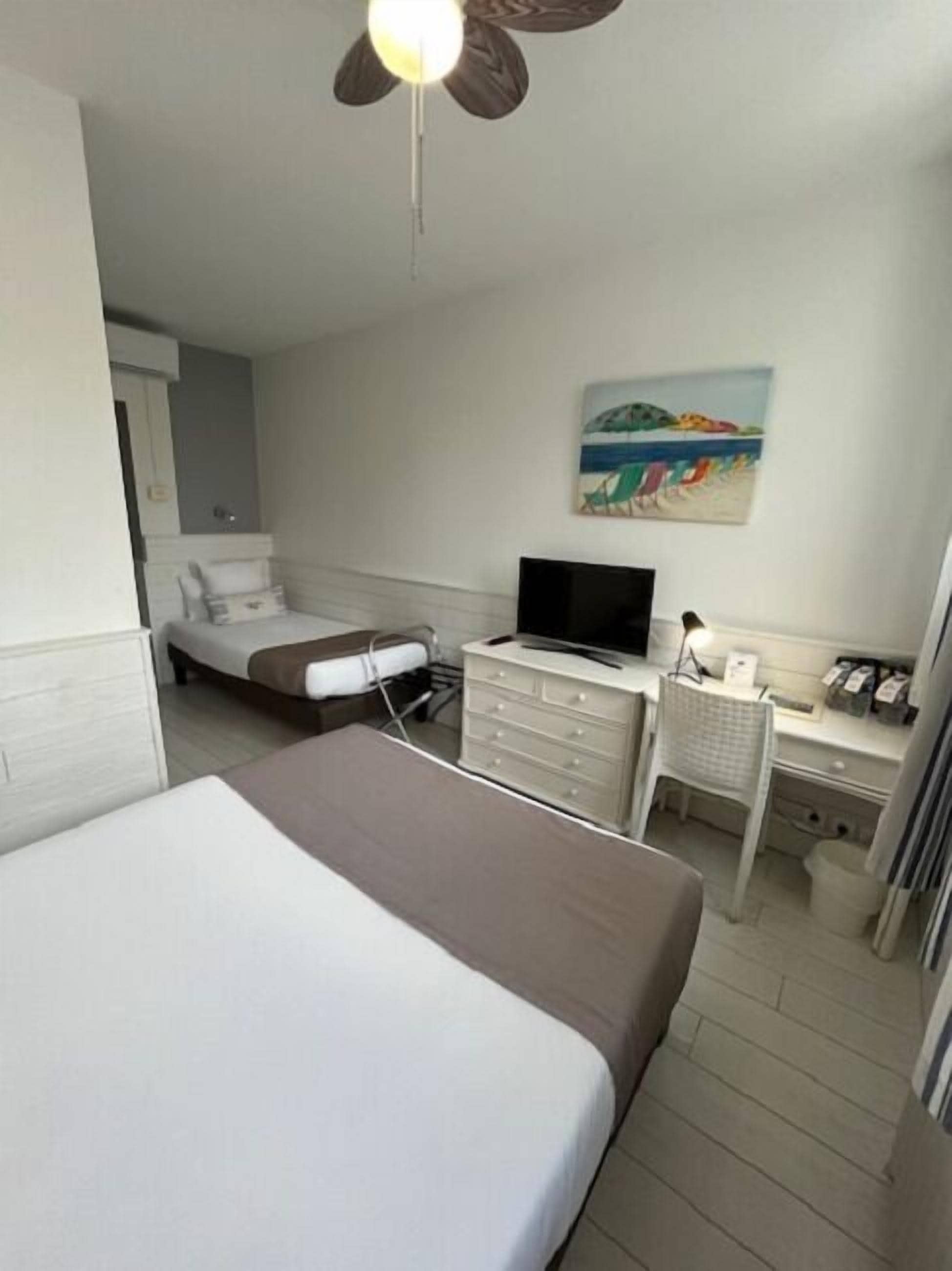 A hotel room with a bed, a desk with a computer, a chair, and a painting on the wall.