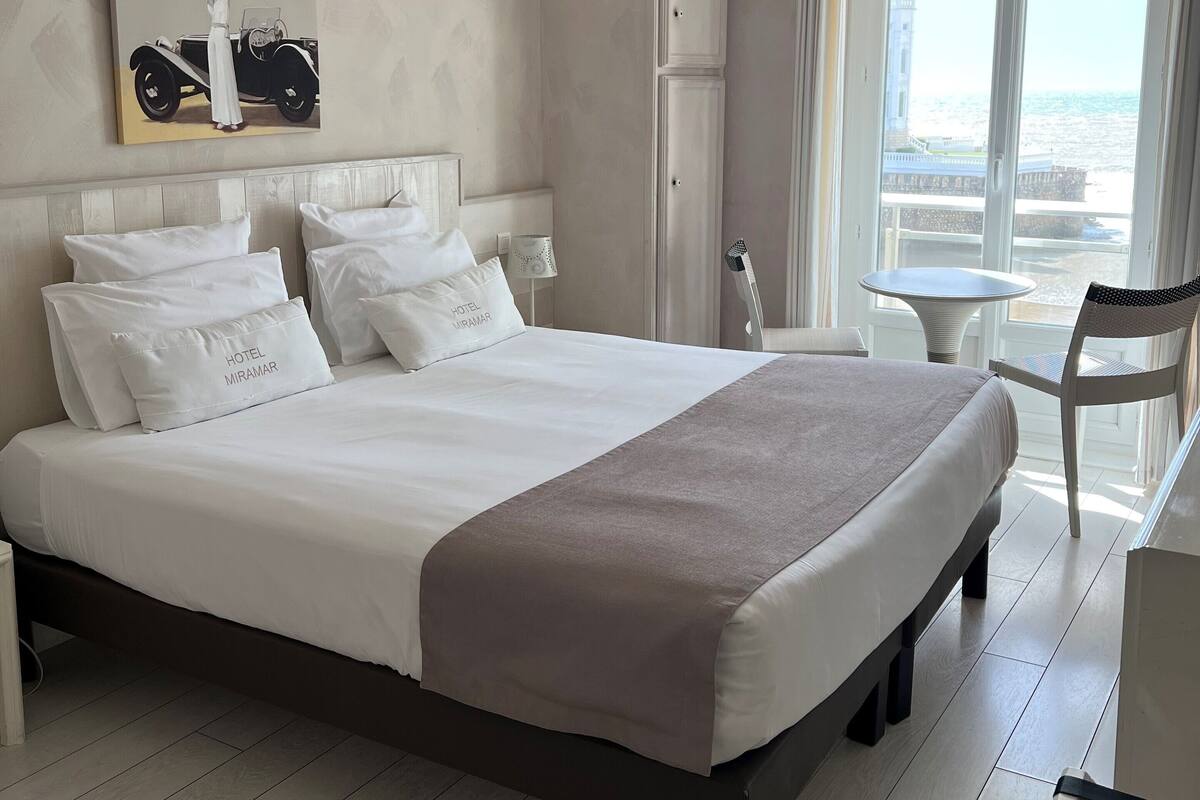 A hotel room with a large bed, a wardrobe, a small table, and a chair.