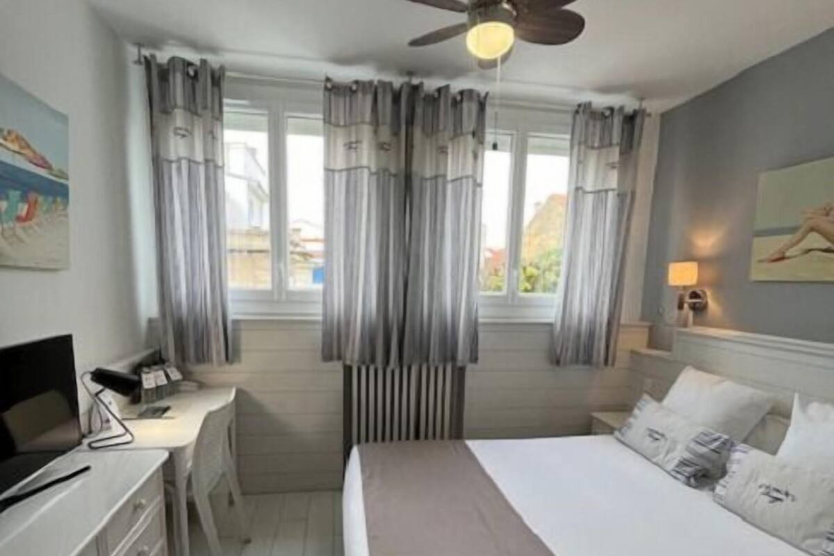 A hotel room with a bed, desk, chair, and a ceiling fan.
