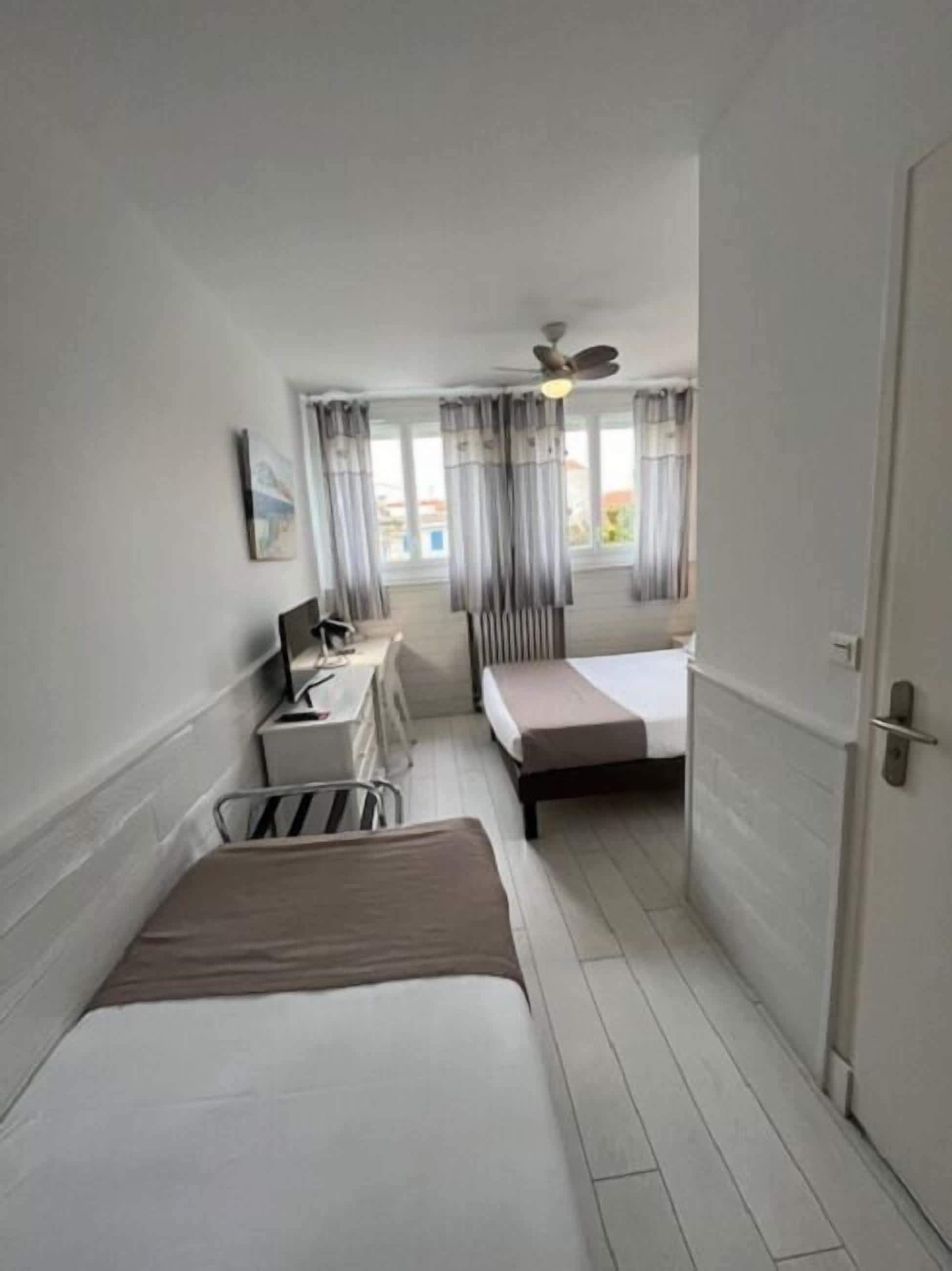 A hotel room with a bed, a desk with a chair, a ceiling fan, and a window with curtains.