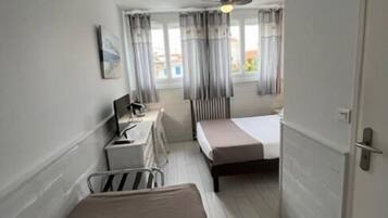 A hotel room with a bed, a desk with a chair, a ceiling fan, and a window with curtains.