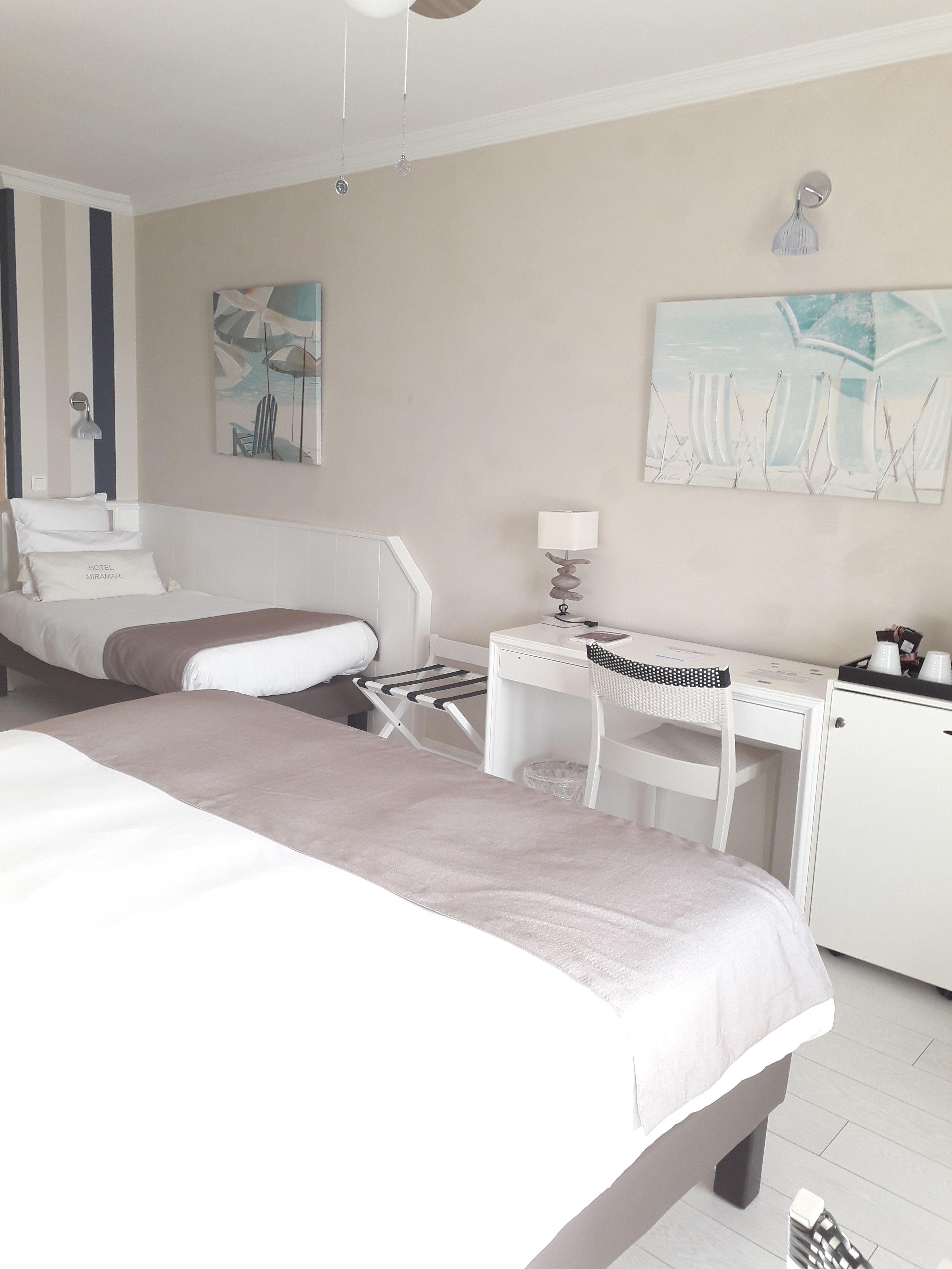 Habitación de hotel con cama, escritorio, silla, lámpara y obras de arte en las paredes.