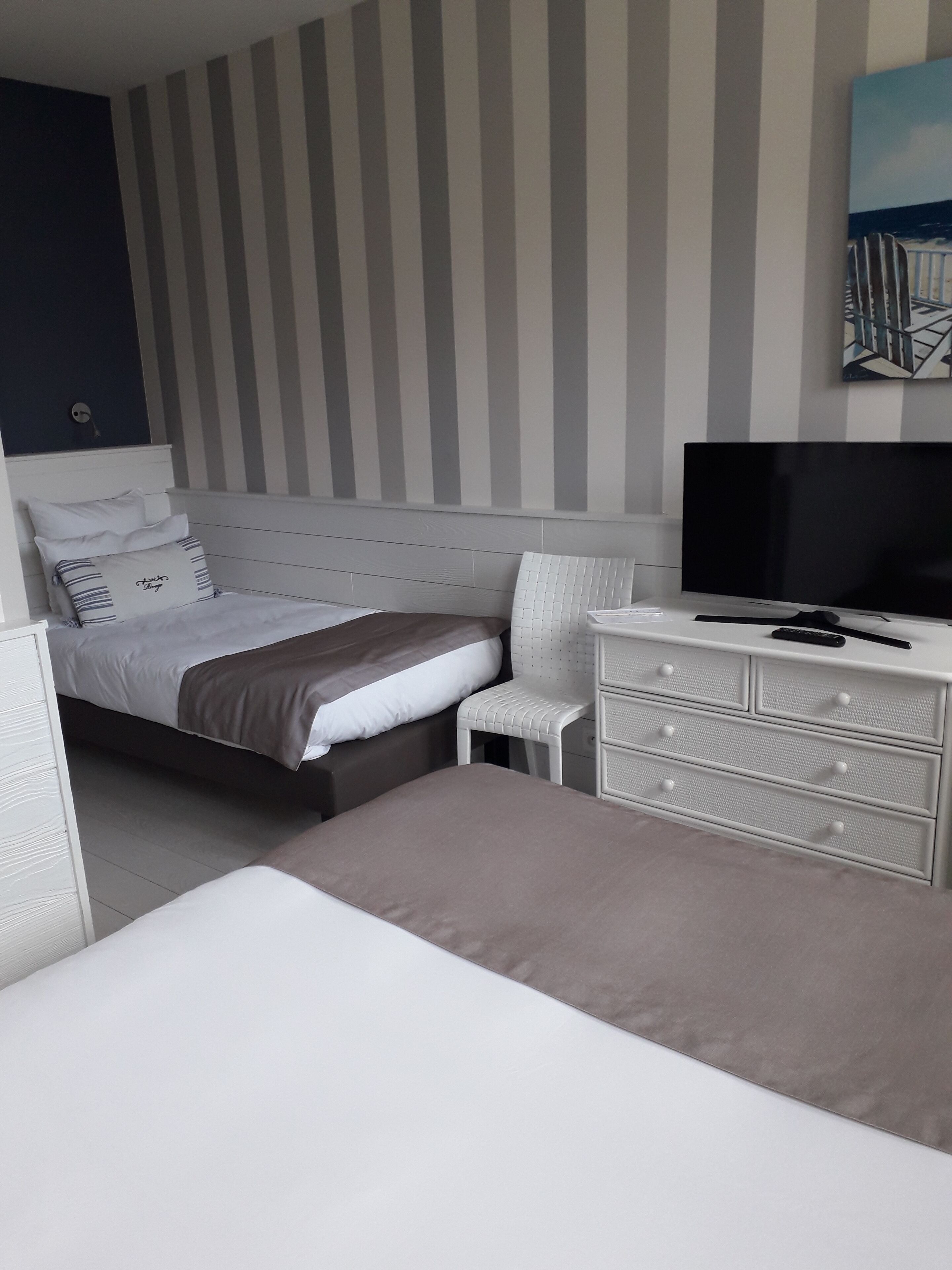 Un dormitorio con cama, televisor, c ómoda y silla.