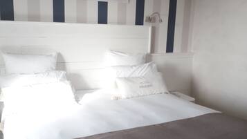 Una cama bien hecha con sábanas blancas y un plaid gris, un cabecero con una obra de arte enmarcada y un estampado a rayas en la pared.
