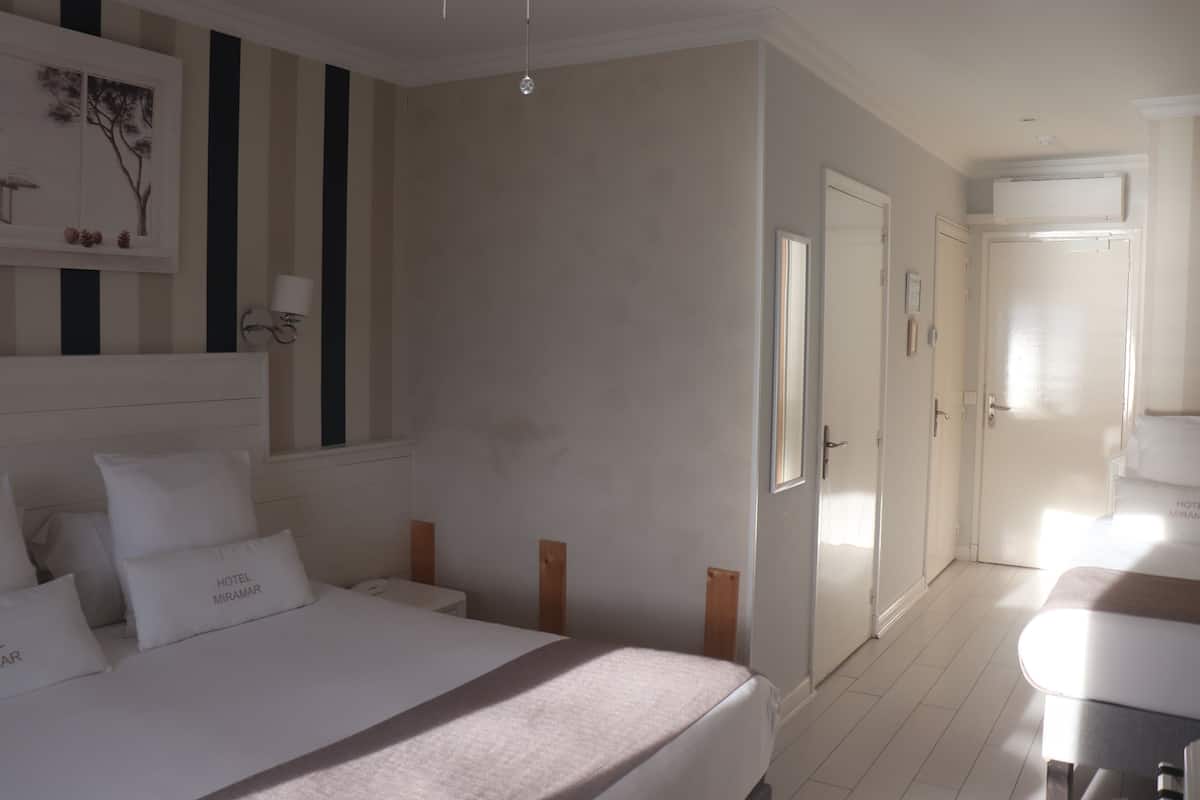 A hotel room with a large bed, bedside tables, a desk, and a chair. There are doors leading to other rooms and a bathroom.