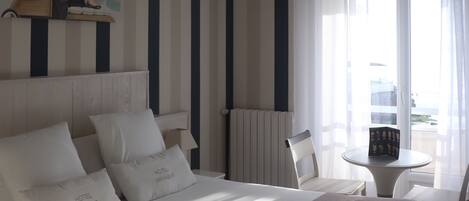 Una habitación de hotel con cama, ventilador de techo, ventana con cortinas, una silla y una mesita.