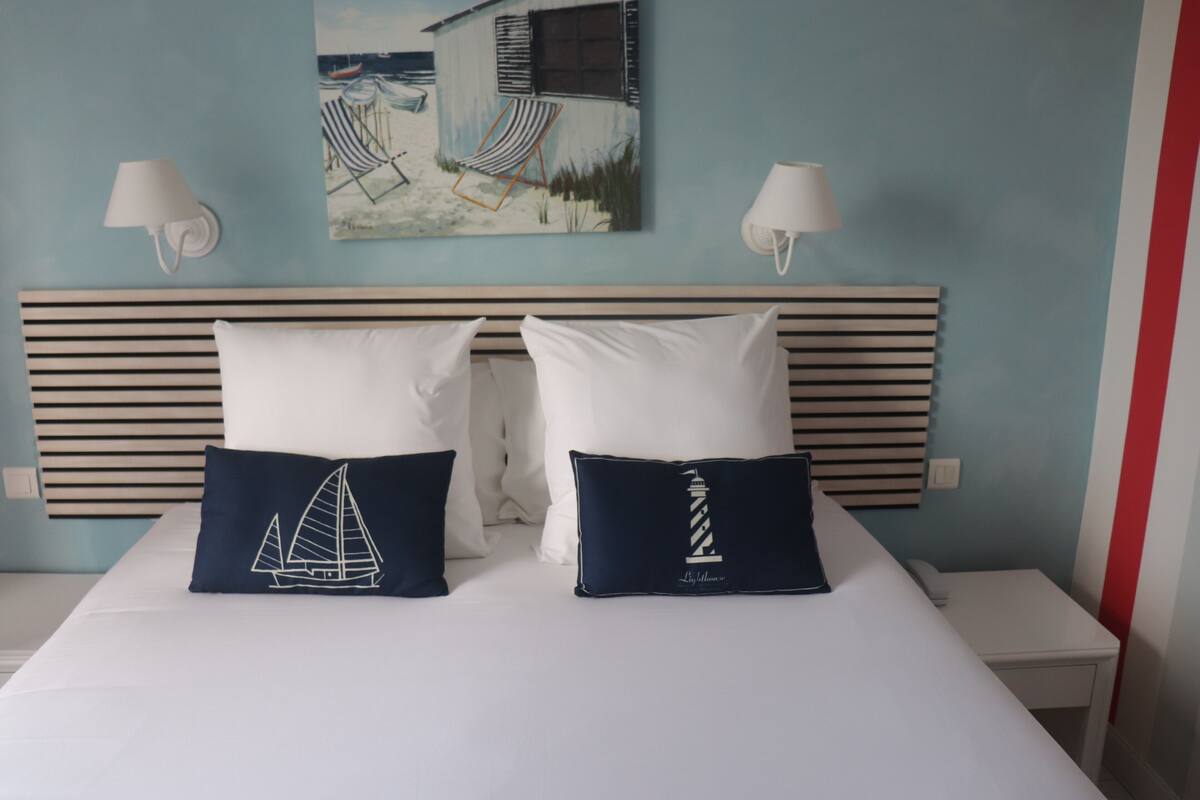 A bed with two pillows, a headboard, and a painting on the wall.