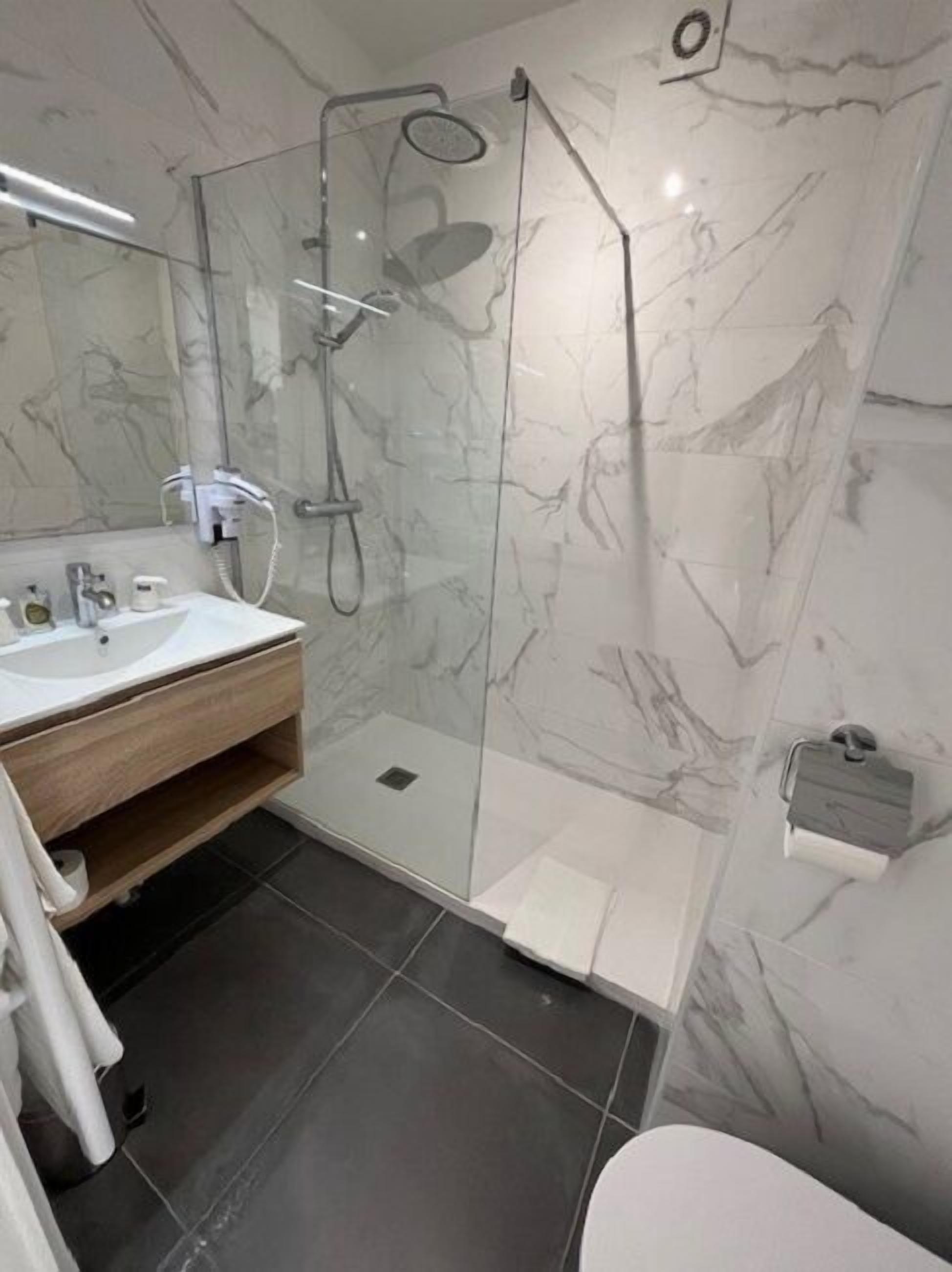 A modern bathroom with a glass-enclosed shower, a wooden vanity, and a marble backsplash.