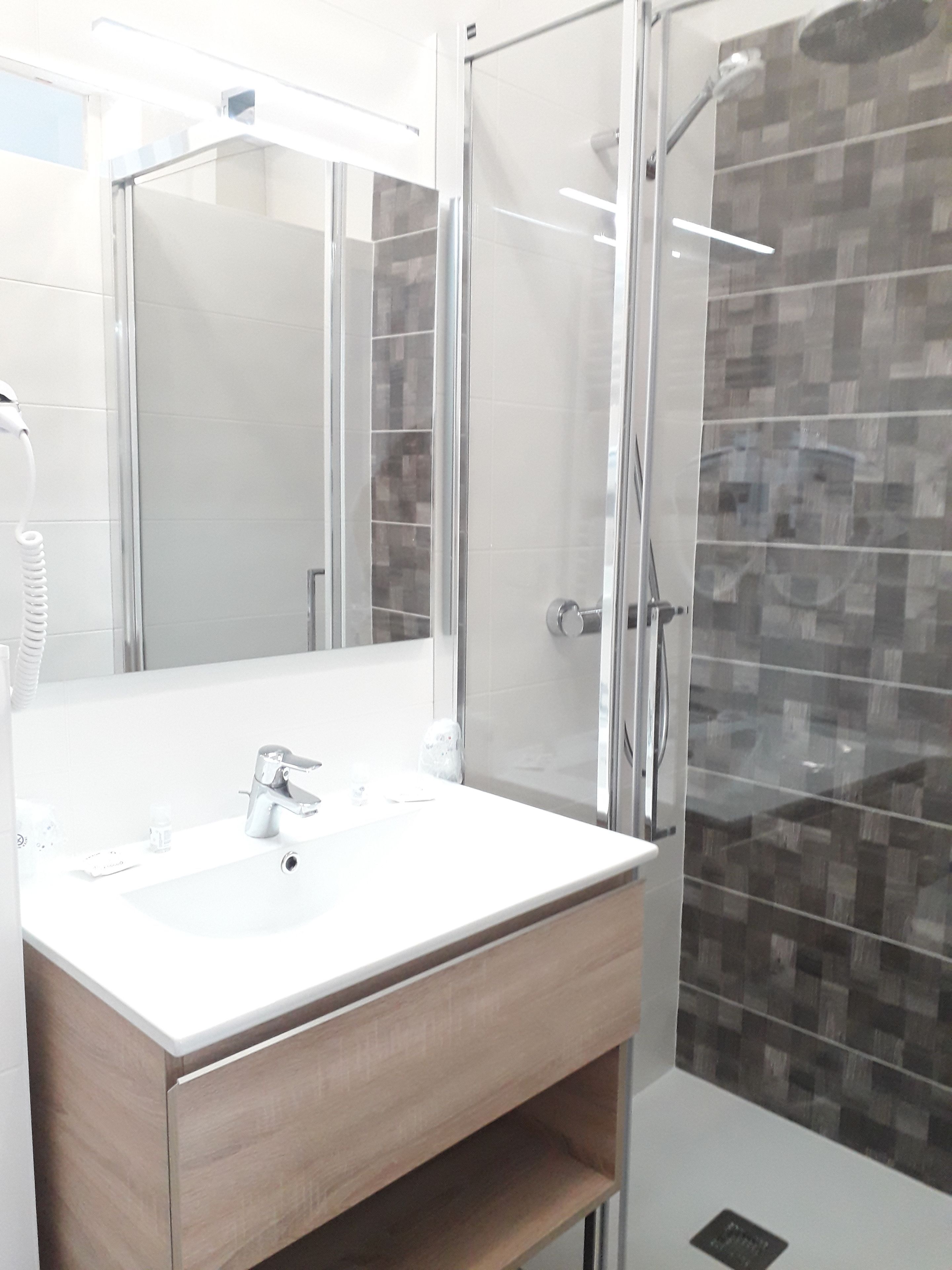 A modern bathroom with a glass shower enclosure, a white sink, and a wooden vanity.