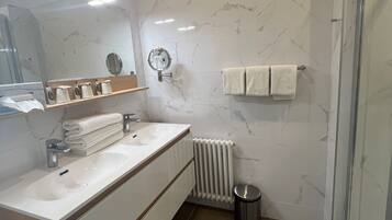 Een moderne badkamer met een marmeren wand, een witte wastafel, een spiegel en een douchecabine van glas.