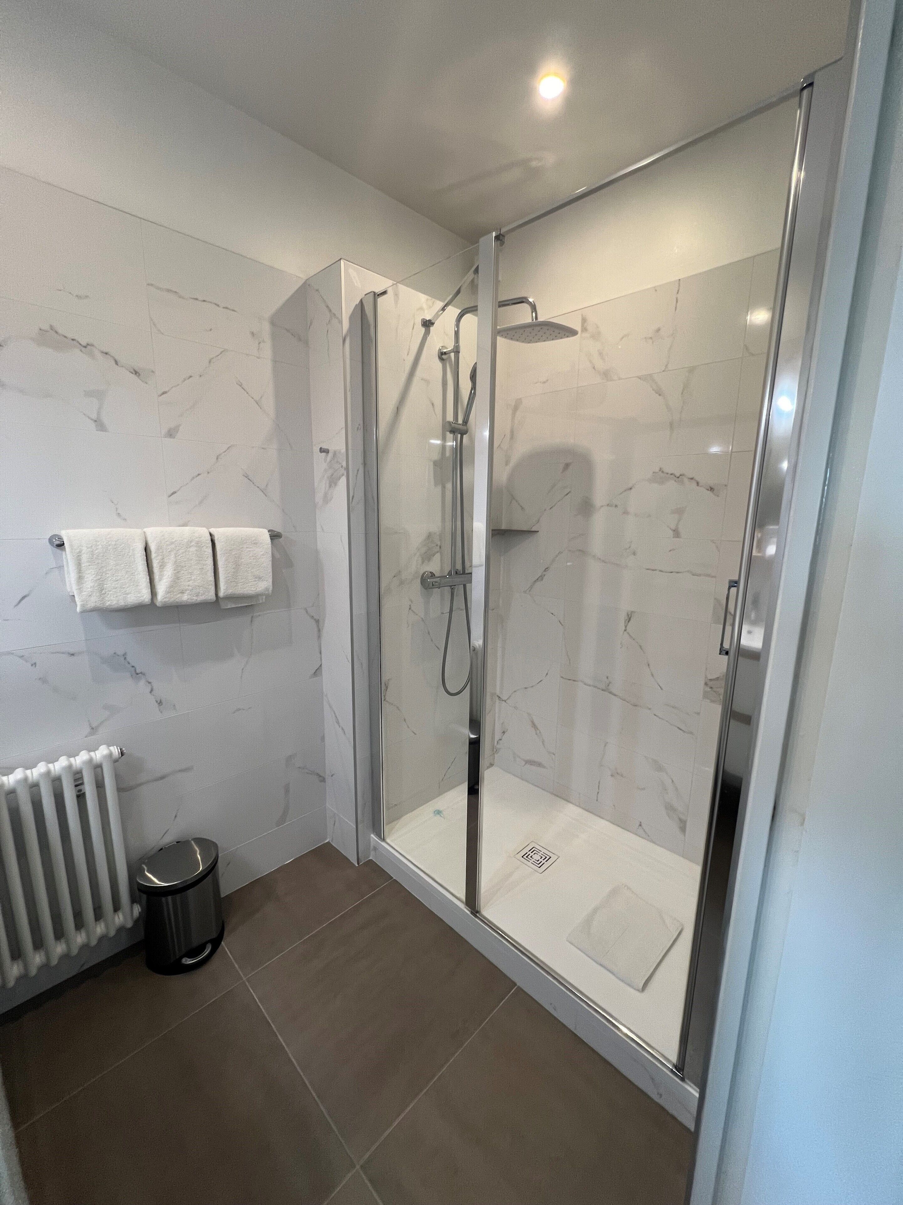 Une salle de bain moderne avec une douche à parois de verre, des carreaux de marbre blanc, un porte-serviettes et un radiateur.