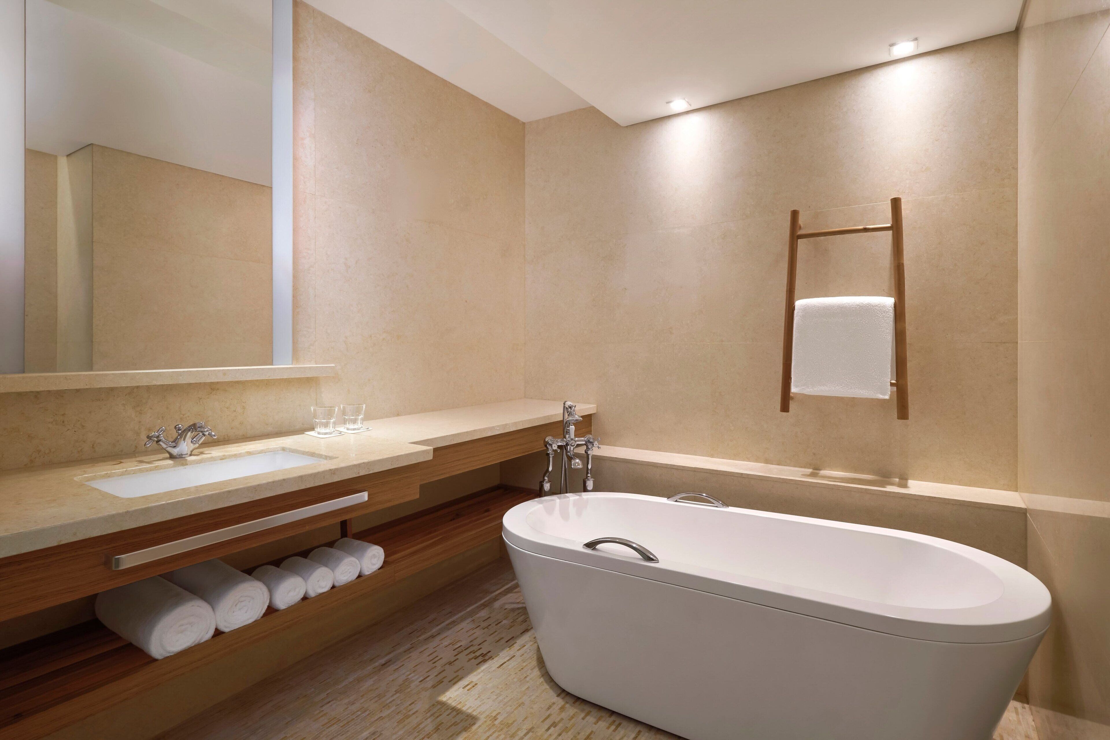 A modern bathroom with a freestanding bathtub, a large mirror, a vanity with a sink, and a towel rack.