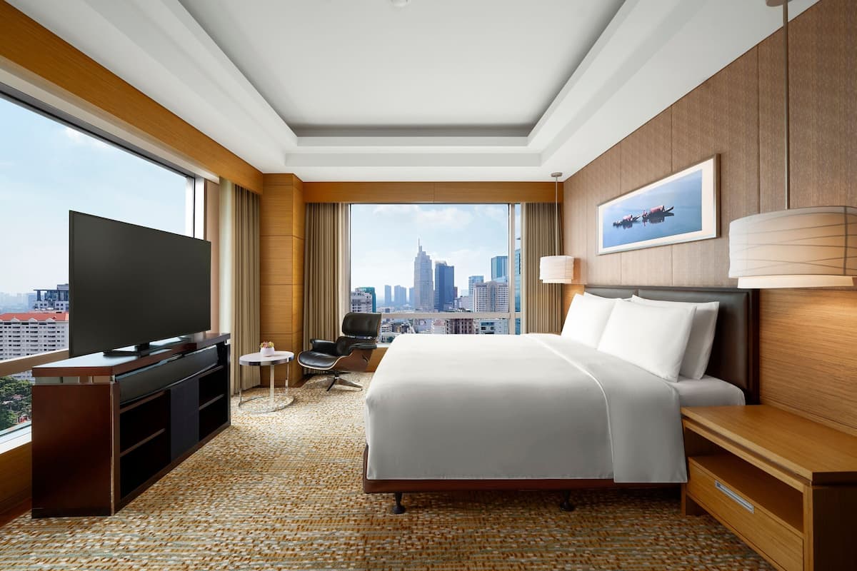 A hotel room with a large bed, a TV, a desk, and a view of the city skyline.