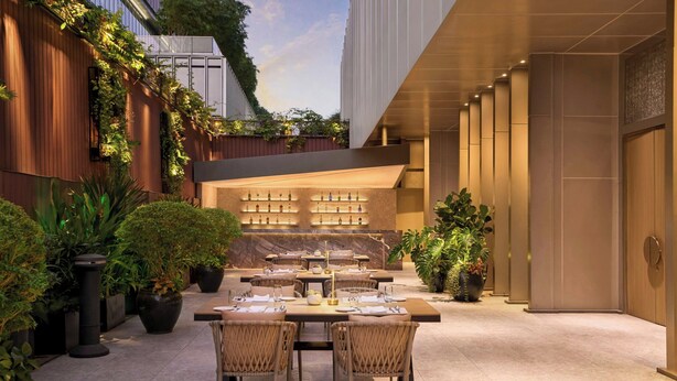 An outdoor dining area with tables and chairs, potted plants, and a bar area with shelves of bottles. - JW Marriott Hotel & Suites Saigon (Ho Chi Minh City)