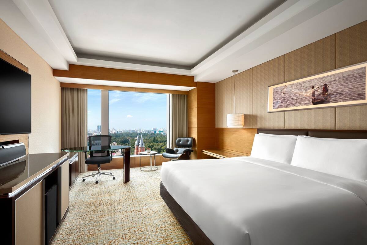 A hotel room with a large bed, a desk with a chair, a television, a window with curtains, and a painting on the wall.