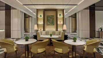 A modern hotel lobby with a central seating area, round tables, and a decorative wall.