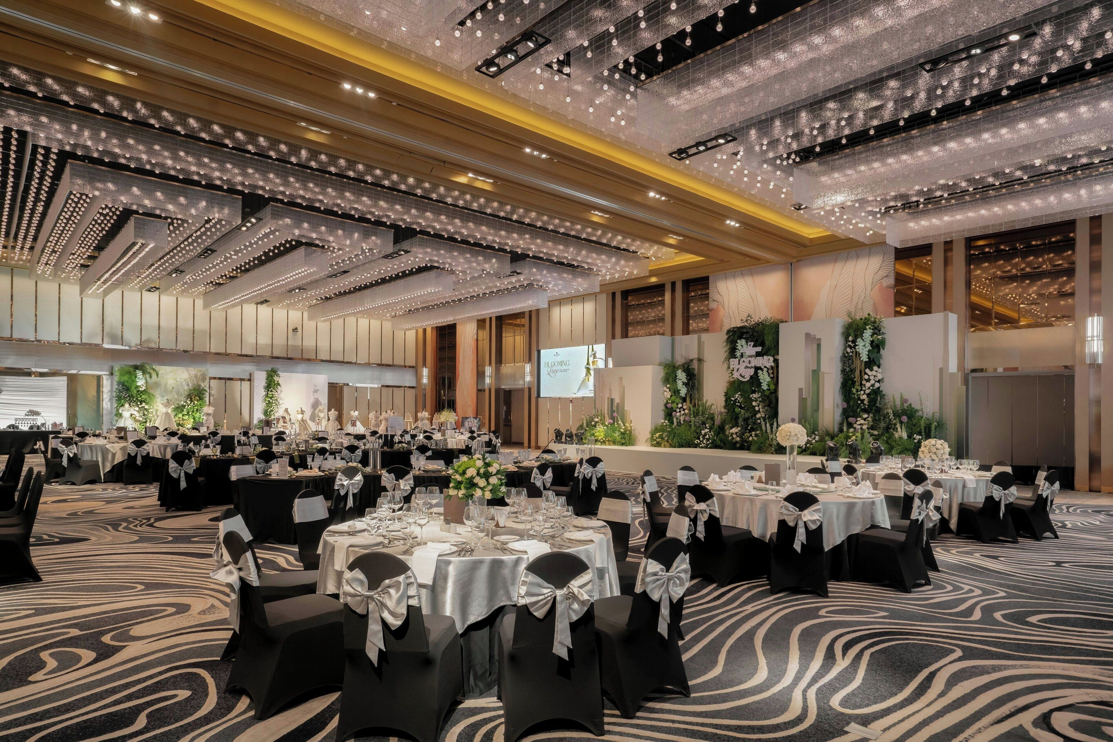 A large banquet hall with round tables set for a formal event, featuring a patterned carpet and modern lighting fixtures.