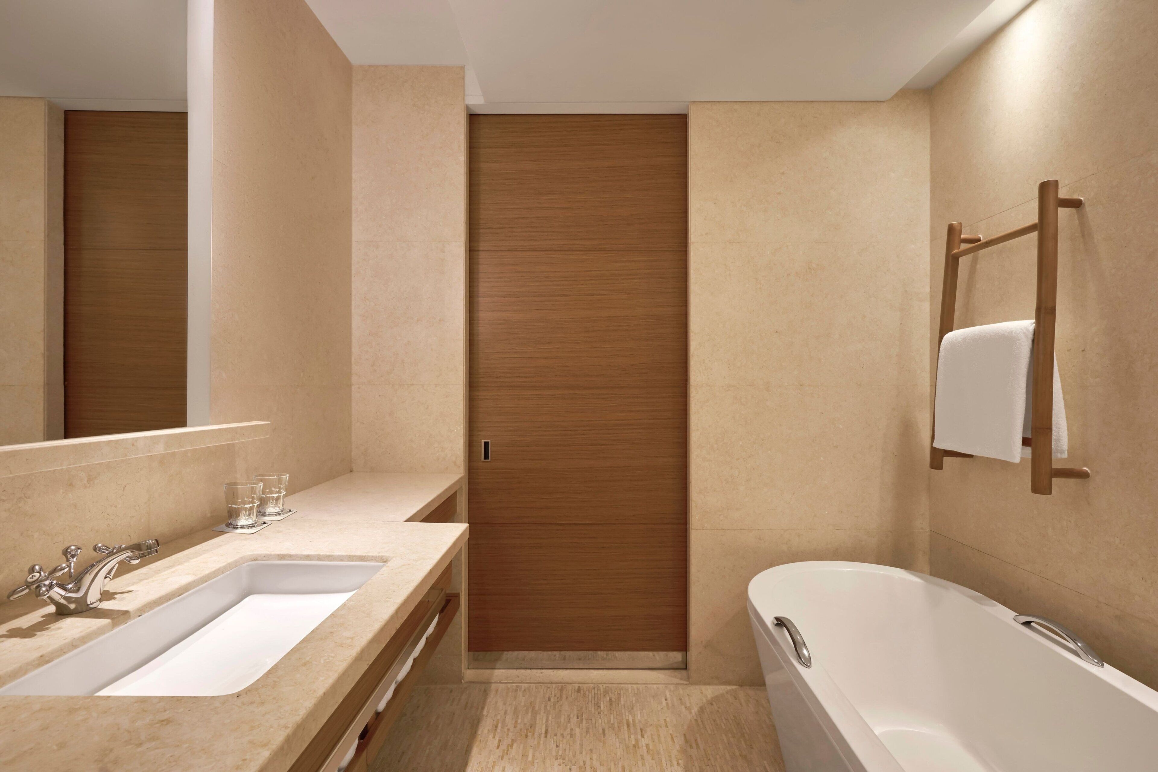 A modern bathroom with a double sink, a bathtub, and a wooden door.