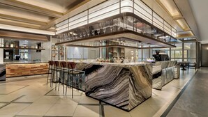 A modern bar area with a marble countertop, bar stools, and a glass-enclosed upper level. - JW Marriott Hotel & Suites Saigon (Ho Chi Minh City)