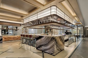 A modern bar area with a marble countertop, bar stools, and a glass-enclosed upper level.