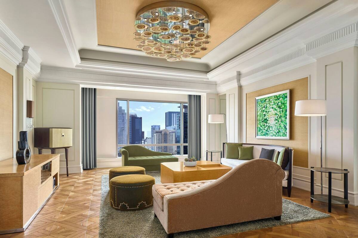 A spacious living room with a large window, a chandelier, a sofa, a coffee table, and a television.