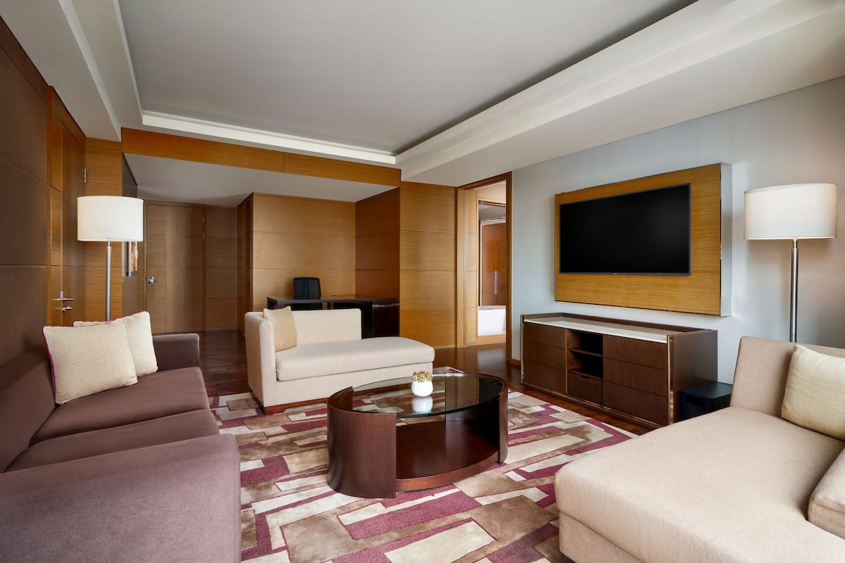 A modern hotel room with a sofa, armchair, and a glass coffee table.