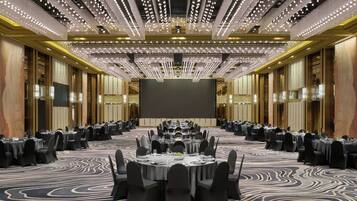 A large conference room with multiple round tables, black chairs, and a large screen at the front.