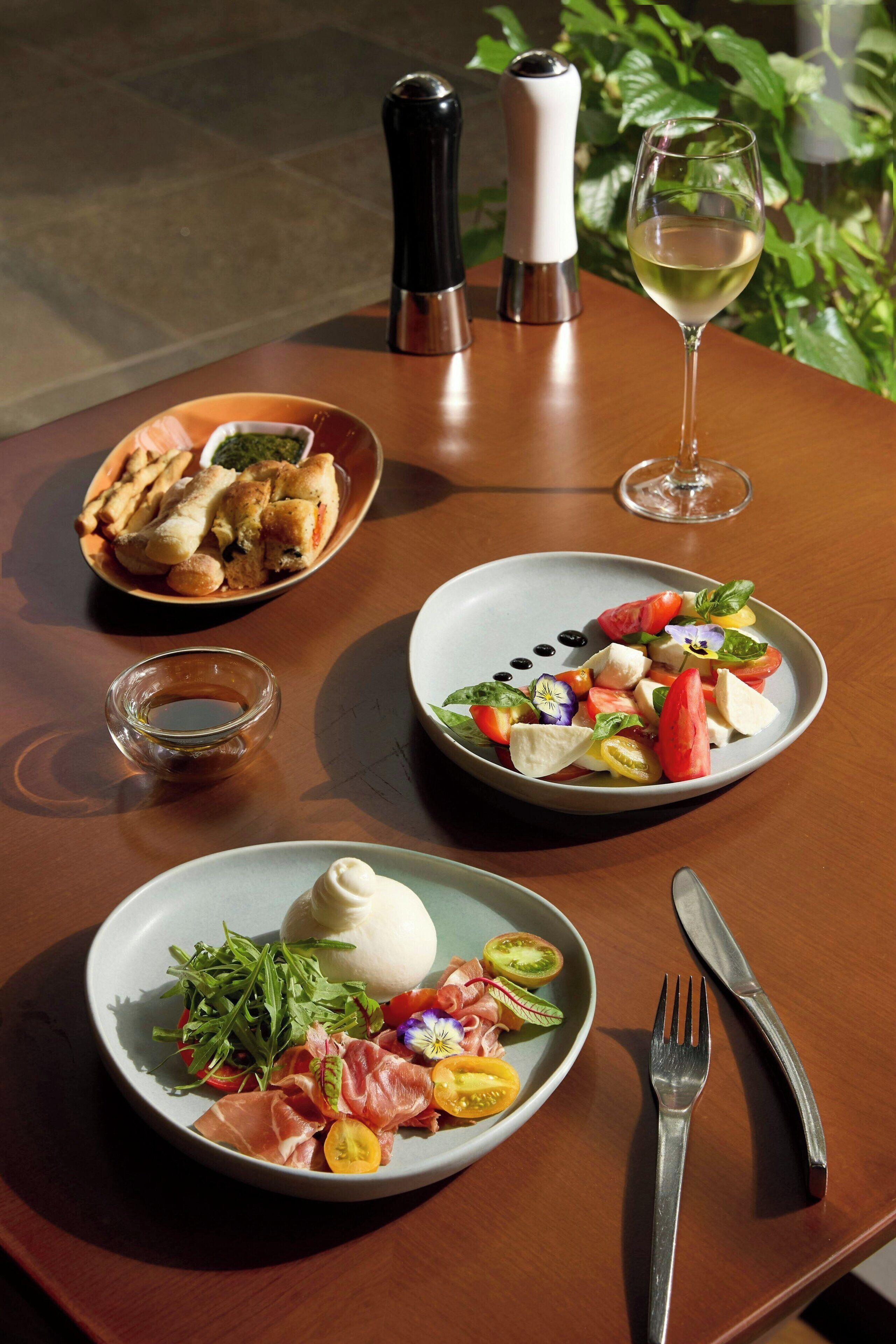 Una mesa con tres platos de comida, una copa de vino y un salero y pimentero.